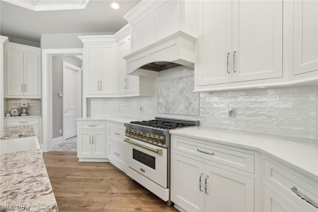 kitchen featuring decorative backsplash, white cabinetry, light hardwood / wood-style floors, high end range, and premium range hood