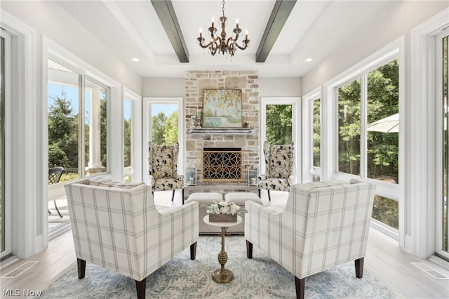 sunroom with a notable chandelier, a fireplace, beamed ceiling, and a wealth of natural light