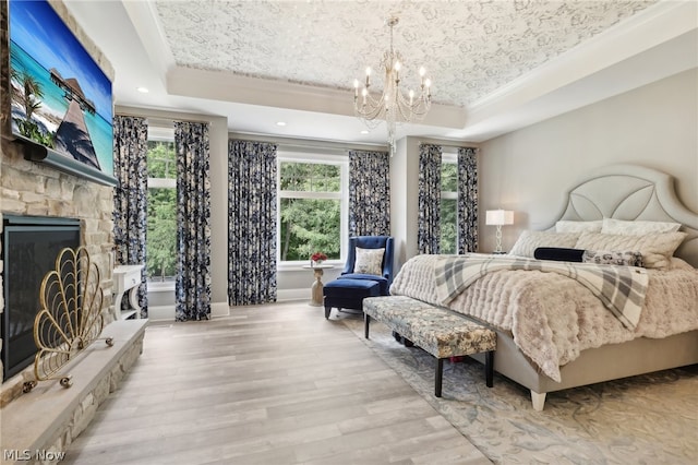 bedroom featuring a stone fireplace, ornamental molding, light hardwood / wood-style floors, a raised ceiling, and a chandelier