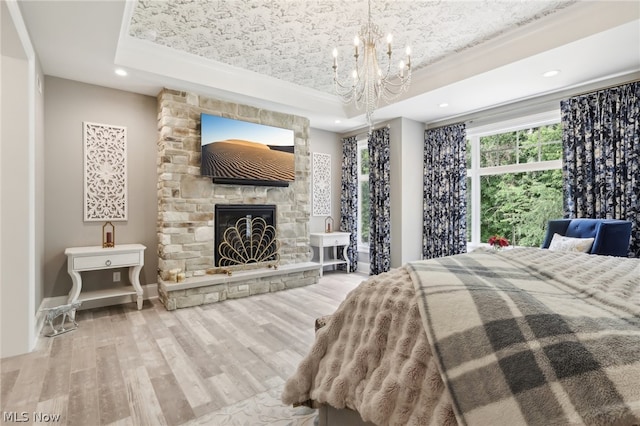 bedroom featuring a notable chandelier, light wood-type flooring, a stone fireplace, and a tray ceiling