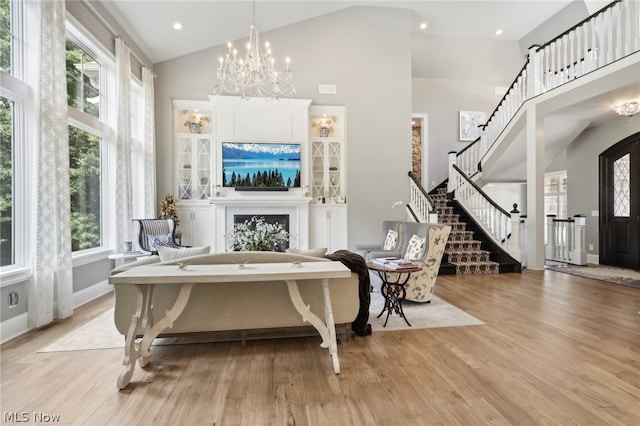 living room with light hardwood / wood-style flooring, high vaulted ceiling, an inviting chandelier, and a wealth of natural light