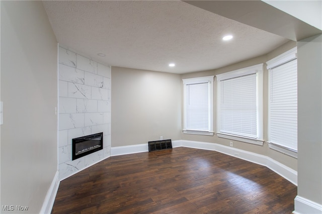 unfurnished living room with a textured ceiling, a tiled fireplace, and dark wood-type flooring