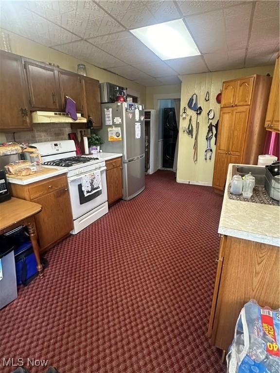 kitchen with carpet floors, white range with gas cooktop, stainless steel refrigerator, a drop ceiling, and premium range hood