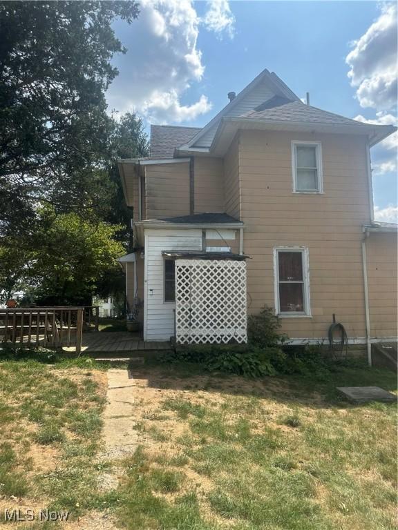 back of property with a wooden deck and a lawn