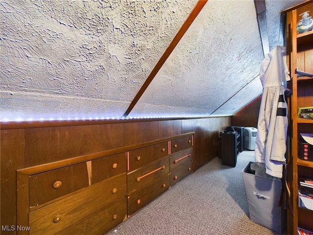 bedroom with wood walls, a textured ceiling, lofted ceiling, and light colored carpet