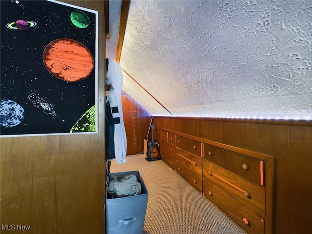 interior space featuring wood walls, a textured ceiling, vaulted ceiling, and light colored carpet