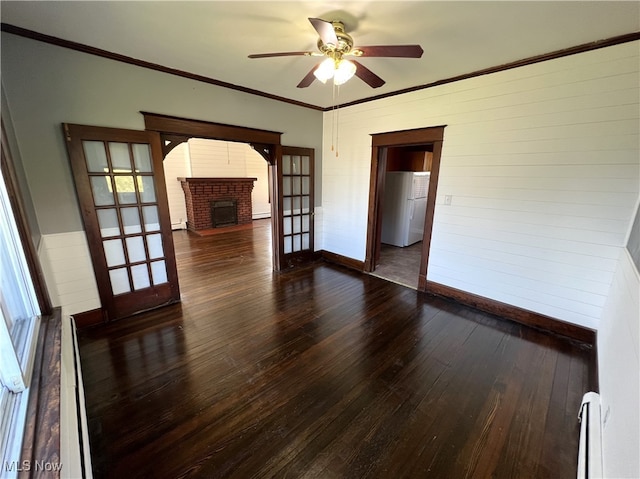 empty room with crown molding, dark hardwood / wood-style flooring, baseboard heating, ceiling fan, and a fireplace