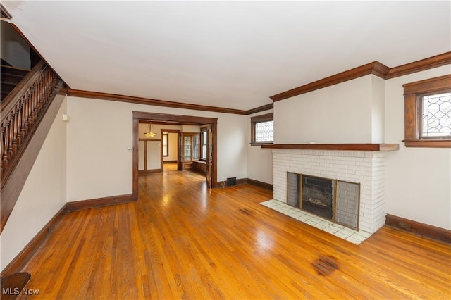 unfurnished living room with wood-type flooring, a brick fireplace, and crown molding