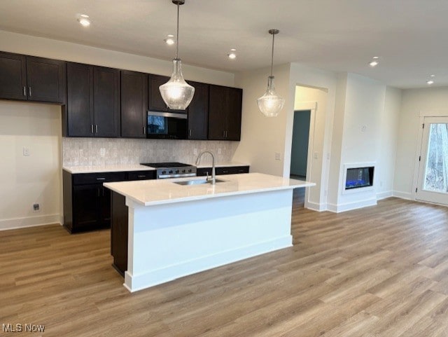 kitchen featuring pendant lighting, sink, decorative backsplash, and a center island with sink