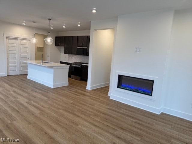 kitchen with hardwood / wood-style floors, hanging light fixtures, stove, a kitchen island with sink, and dark brown cabinetry