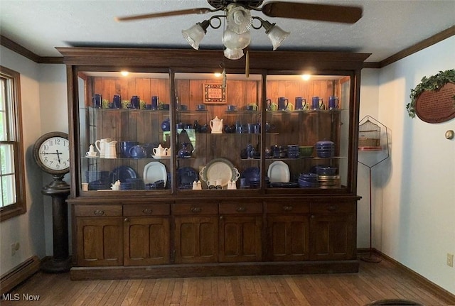 bar with crown molding, light wood-type flooring, ceiling fan, and baseboard heating