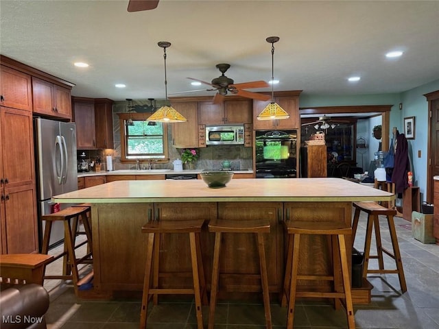 kitchen with pendant lighting, ceiling fan, appliances with stainless steel finishes, a kitchen island, and decorative backsplash