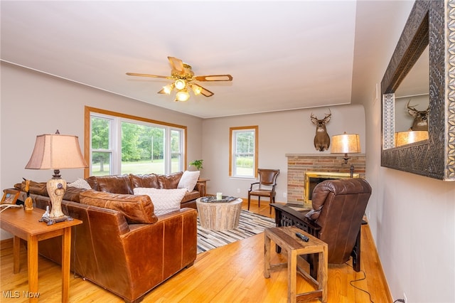 living room with light hardwood / wood-style floors, ceiling fan, and a brick fireplace