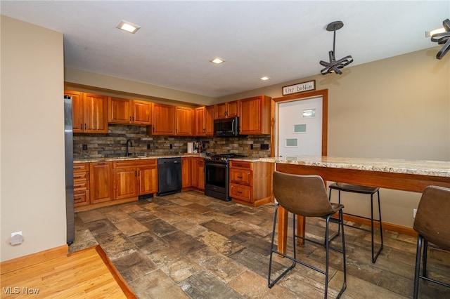 kitchen featuring backsplash, sink, wood-type flooring, light stone countertops, and black appliances