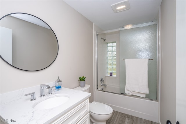 full bathroom featuring hardwood / wood-style flooring, bath / shower combo with glass door, toilet, and vanity