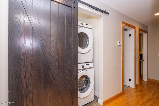 laundry area featuring light wood-type flooring, a barn door, and stacked washer and dryer