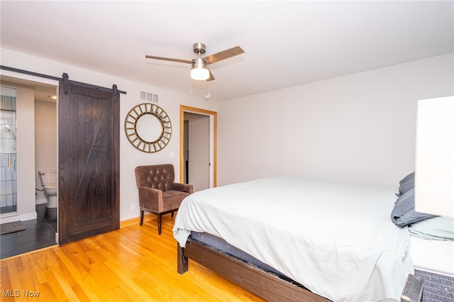 bedroom with ceiling fan, ensuite bath, light hardwood / wood-style floors, and a barn door