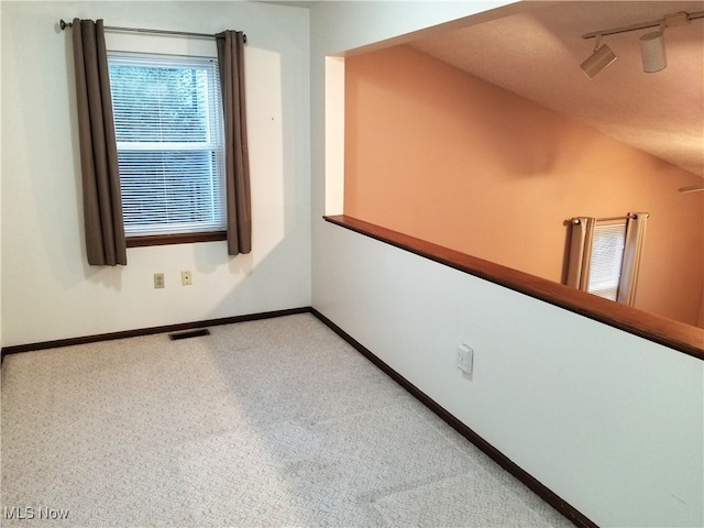 carpeted spare room featuring vaulted ceiling and rail lighting