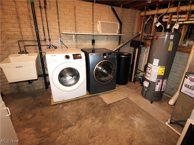 washroom featuring water heater, brick wall, sink, and washing machine and clothes dryer