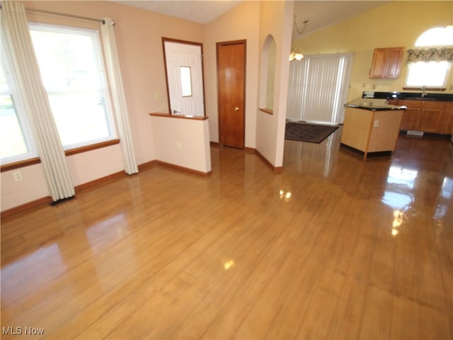 unfurnished living room with hardwood / wood-style floors, sink, a chandelier, and vaulted ceiling