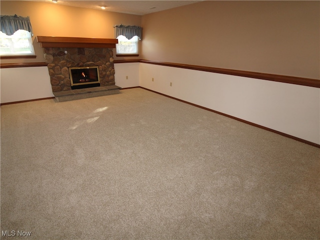 unfurnished living room featuring a stone fireplace, plenty of natural light, and light carpet