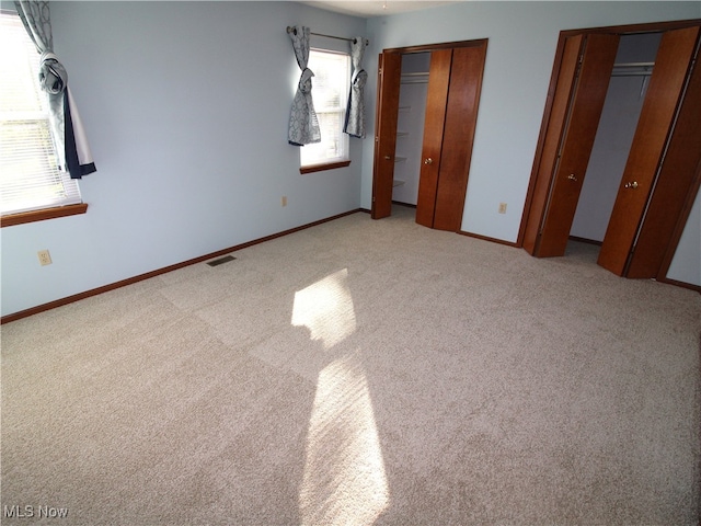 unfurnished bedroom with light carpet, multiple windows, and two closets