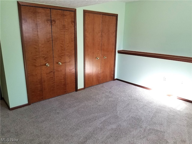 unfurnished bedroom featuring multiple closets, a textured ceiling, and light carpet