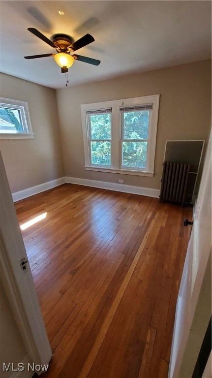 unfurnished room with ceiling fan, radiator, and wood-type flooring