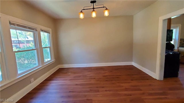 spare room featuring dark wood-style floors, an inviting chandelier, and baseboards