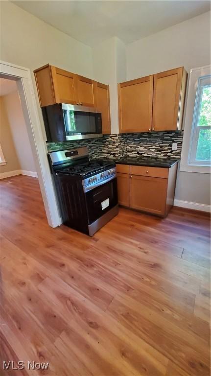 kitchen with appliances with stainless steel finishes, backsplash, and light hardwood / wood-style flooring