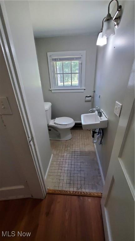 half bath featuring wood finished floors, a sink, and toilet