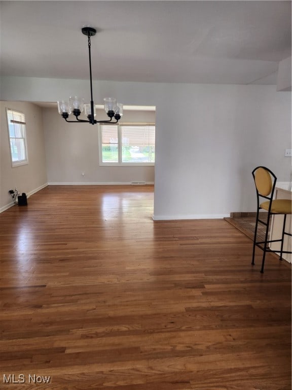 unfurnished dining area with dark wood finished floors, a wealth of natural light, and an inviting chandelier