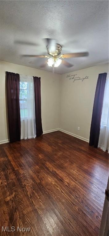 spare room featuring dark wood-style floors, a textured ceiling, baseboards, and a ceiling fan