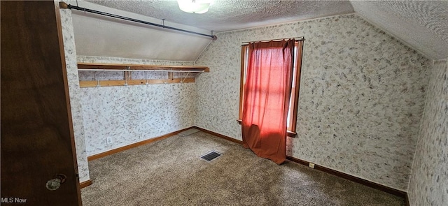 additional living space with wallpapered walls, visible vents, lofted ceiling, a textured ceiling, and carpet floors