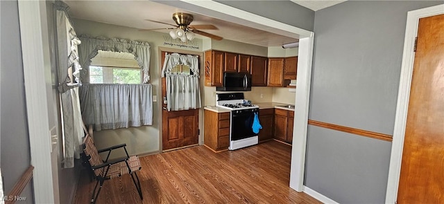 kitchen with brown cabinets, light countertops, black microwave, wood finished floors, and white range with gas stovetop