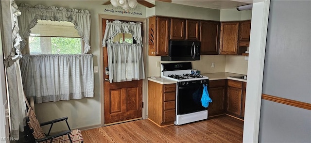 kitchen with gas range, light wood-style flooring, ceiling fan, light countertops, and black microwave