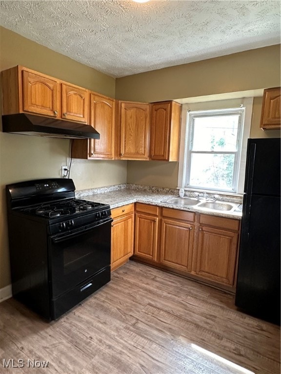 kitchen with light wood-type flooring, black appliances, a textured ceiling, and sink