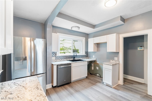 kitchen with light wood-type flooring, light stone counters, white cabinets, sink, and appliances with stainless steel finishes