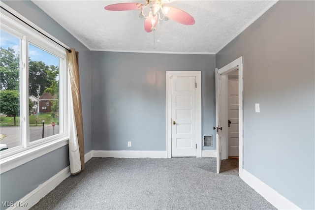 unfurnished bedroom featuring ceiling fan, carpet, ornamental molding, and a textured ceiling