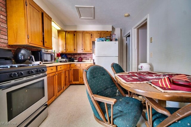 kitchen with gas range, decorative backsplash, a textured ceiling, light tile patterned flooring, and white refrigerator