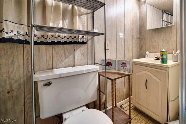 bathroom featuring tile patterned flooring, wooden walls, vanity, and toilet