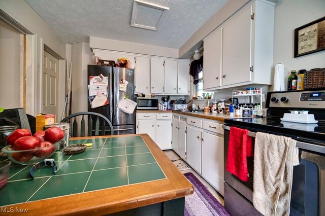 kitchen with appliances with stainless steel finishes, tile countertops, and white cabinets