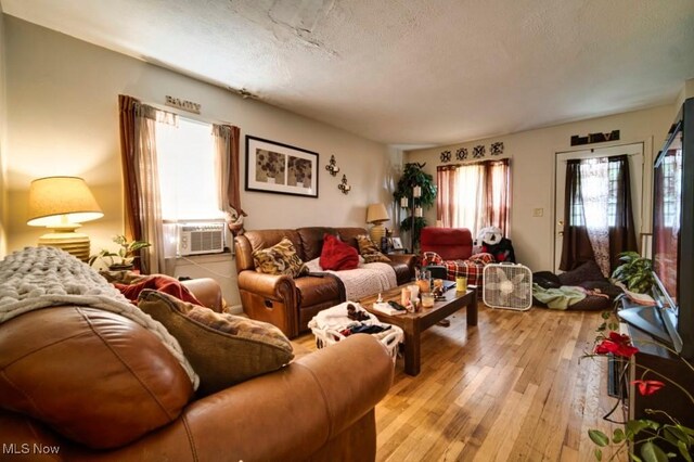 living room with a textured ceiling, plenty of natural light, cooling unit, and light wood-type flooring