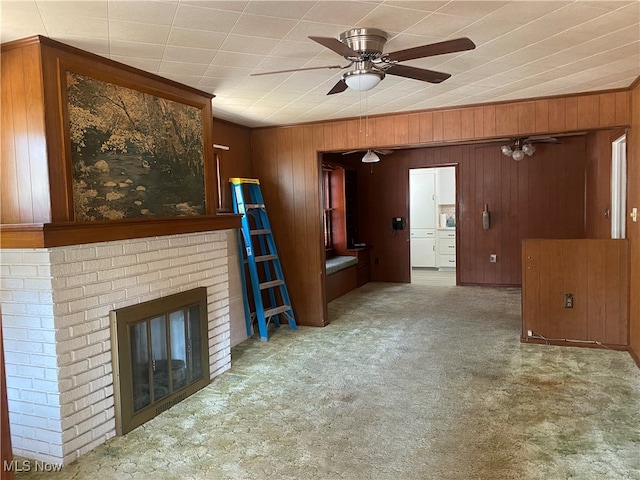 unfurnished living room featuring wood walls, ceiling fan, carpet floors, and a fireplace