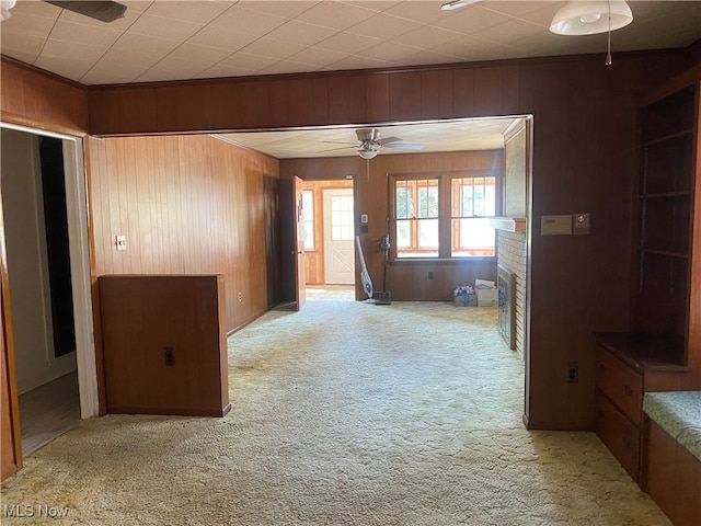 interior space with wooden walls, ceiling fan, light colored carpet, and a brick fireplace