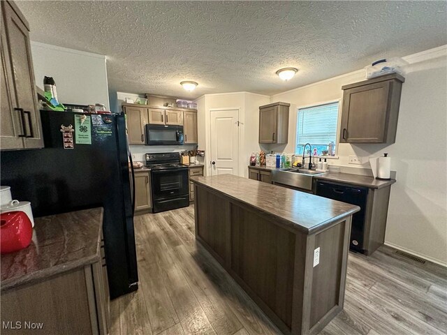 kitchen featuring visible vents, light wood-style flooring, a kitchen island, a sink, and black appliances