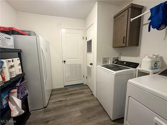 washroom with dark wood-style flooring, cabinet space, visible vents, ornamental molding, and washing machine and dryer