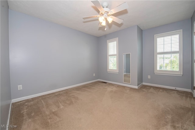 unfurnished room featuring ceiling fan, a wealth of natural light, and light carpet