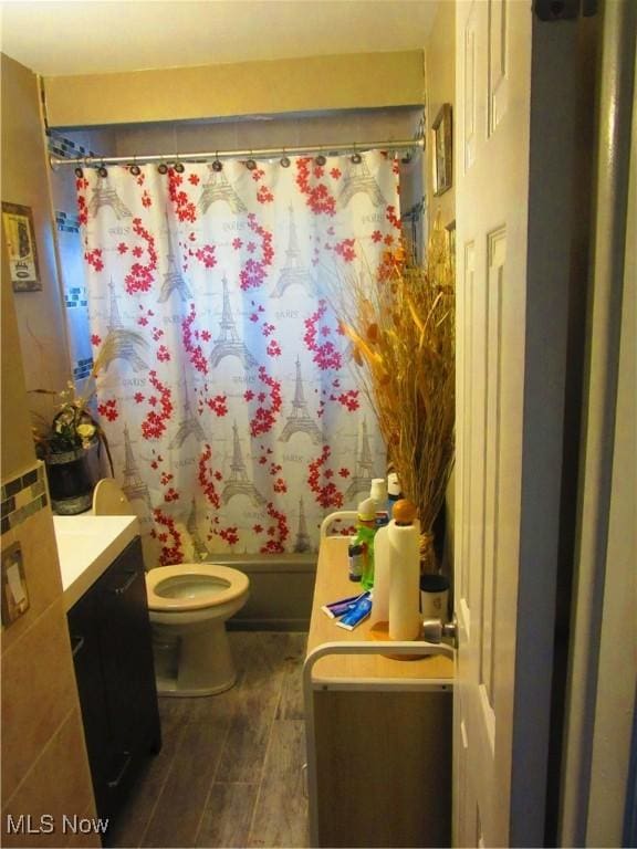 full bath with toilet, shower / bath combo with shower curtain, wood finished floors, and vanity