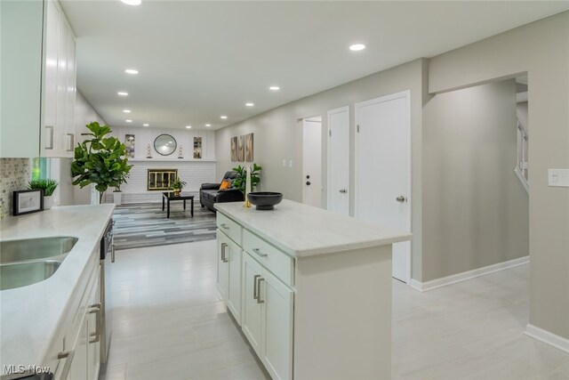 kitchen with a center island, light wood-type flooring, light stone counters, tasteful backsplash, and white cabinets